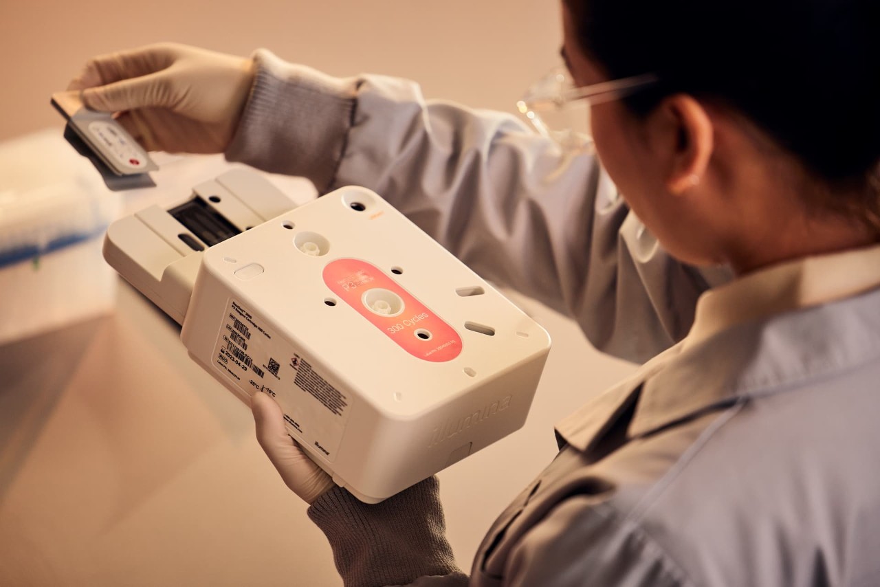 Scientist, back view, removing gray tab protective coving over flow cell from NextSeq 1000/2000 P3 reagent cartridge, 300 cycles