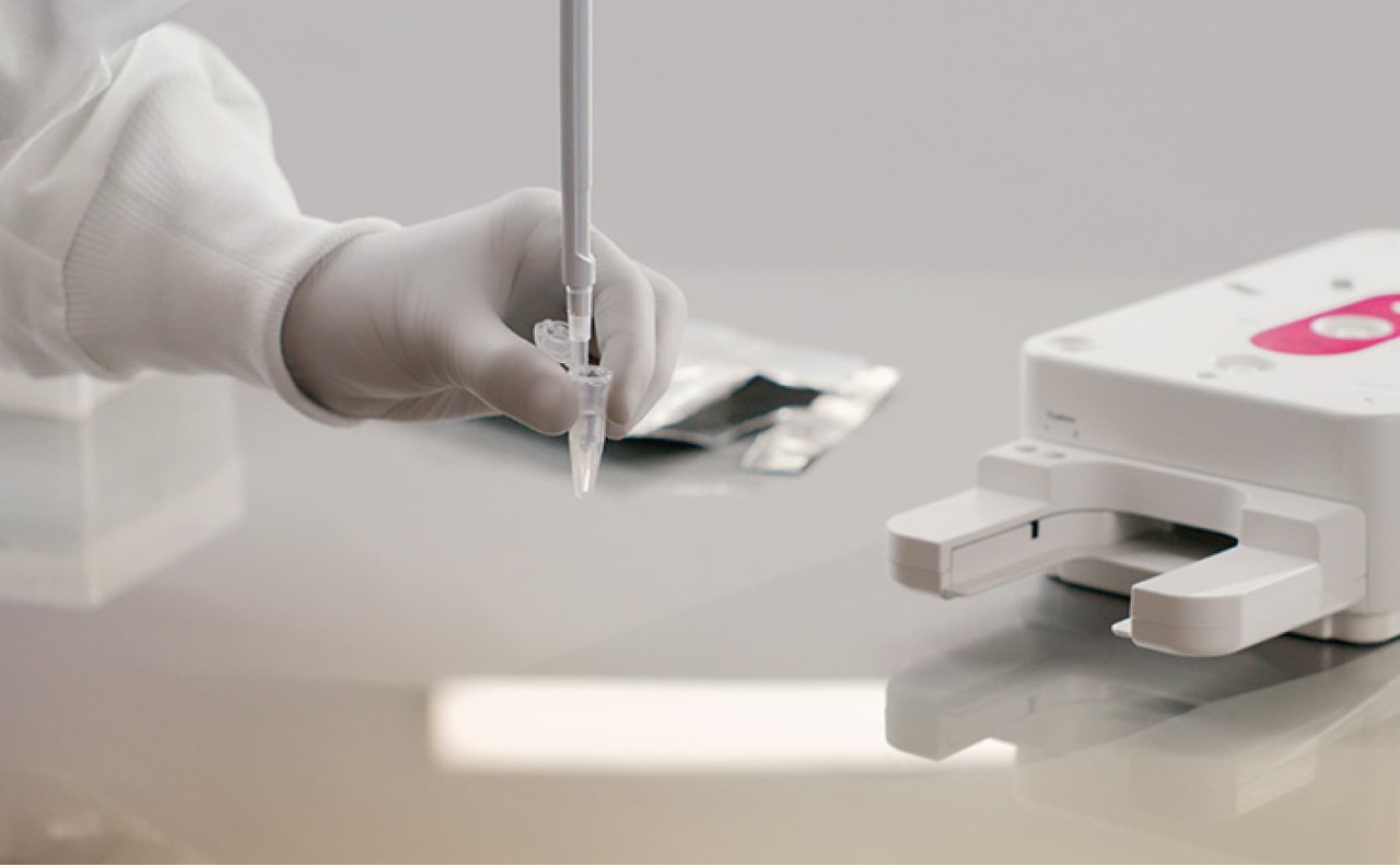 On a lab bench, a scientist pipetting using a single channel tube, filled, part of a library prep workflow. Reagent cartridge and tray in the background.