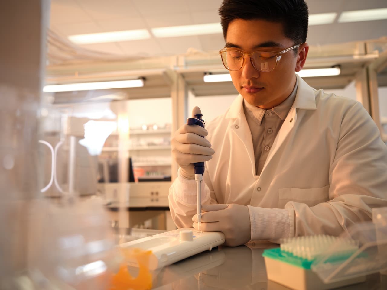 Front view of a male scientist using a single pipette preparing the flow cell for loading in a lab. Tube container is in the foreground.